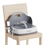 Rehausseur de chaise bébé gris sanglé sur une chaise en bois clair
